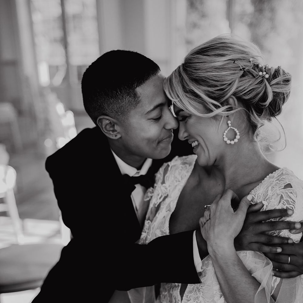 LGBTQI+ couple embracing at Hodscok Priory with bride in a lace wedding dress with pinned up with pearl slides 