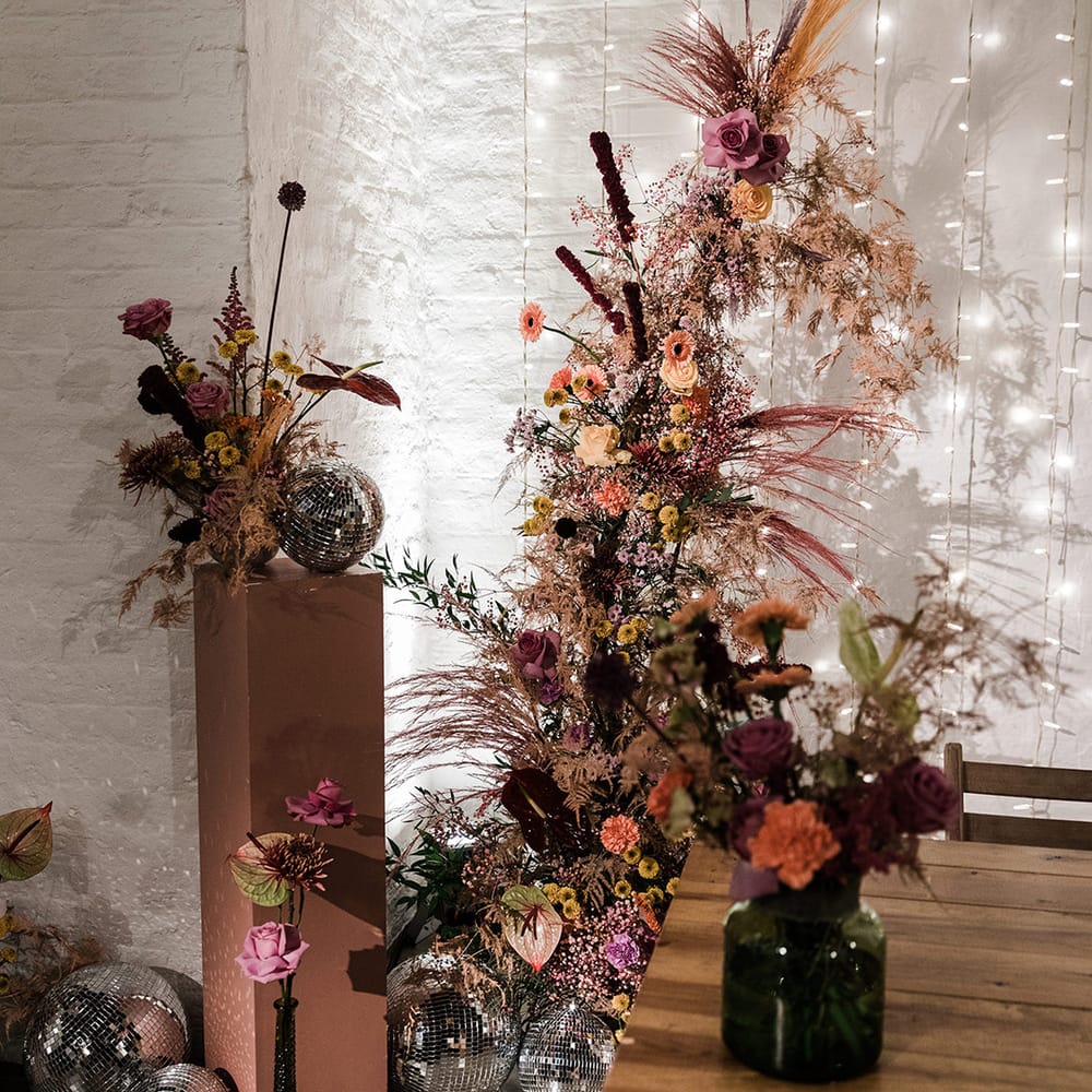 Purple and orange flowers in vases and in a flower column with disco balls and fairy light back drop for wedding reception decor |