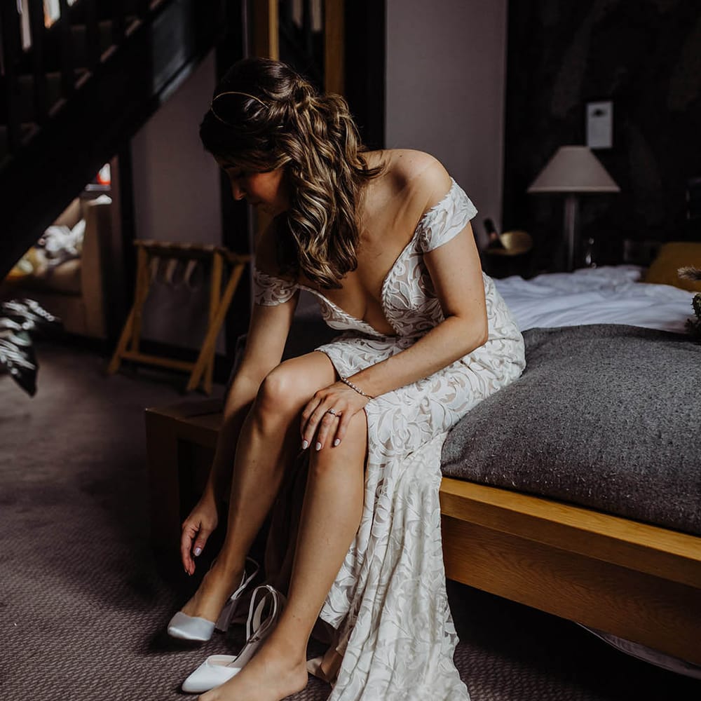 Bride in lace wedding dress putting on her white wedding heels 