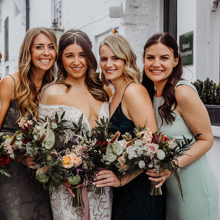 Bride with bridesmaids in a variety of shades of green and bride in a boho style wedding look with gold headband and fitted lace dress
