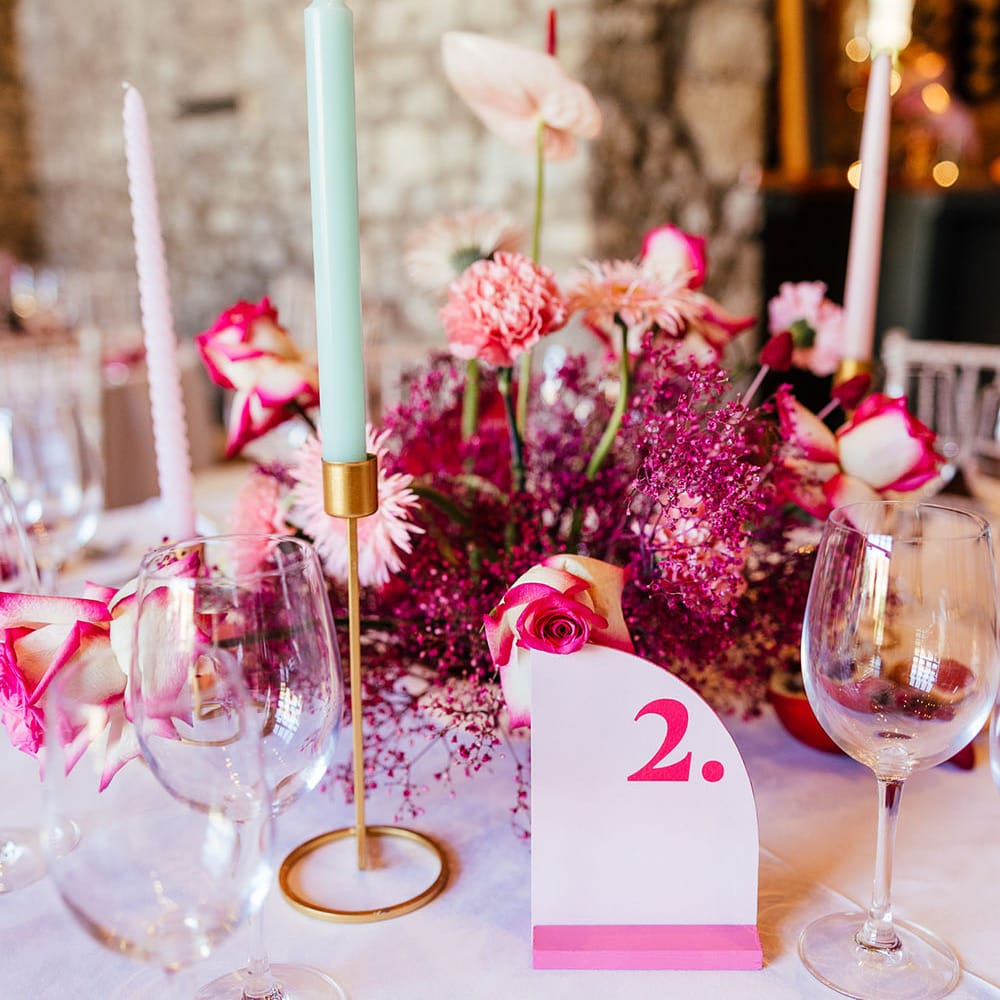 Bright pink floral centrepiece surrounded by pastel candles and dried fruit decor for modern tablescape 