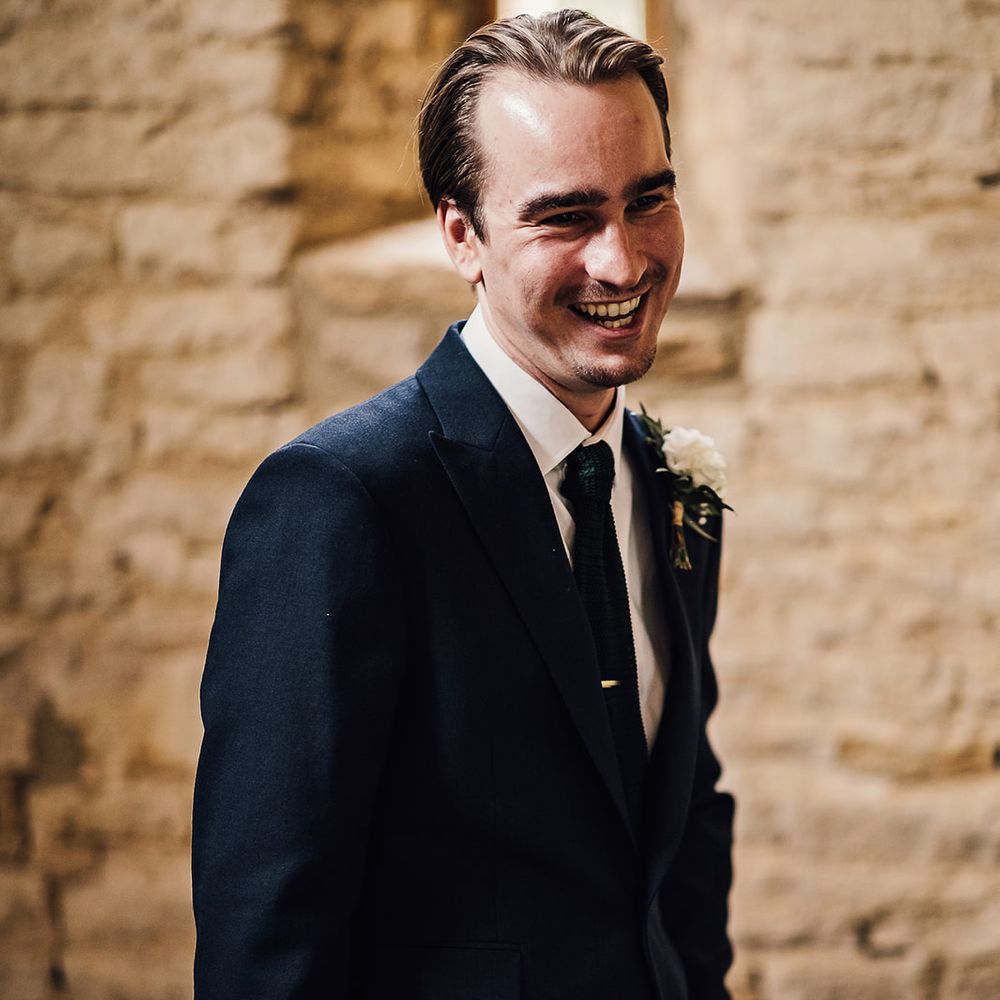 Smiling groom in a navy blue suit with a white rose buttonhole 
