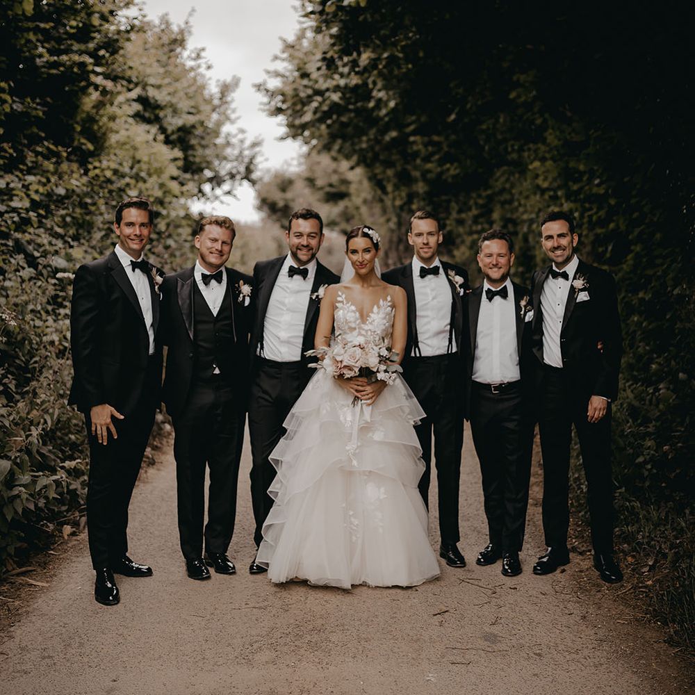 The bride in a Wtoo by Watters wedding dress stands with the groom and groomsmen in black tie