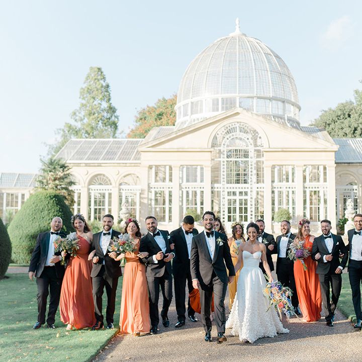 Bride & groom walk with their wedding party outside Syon Park Conservatory 