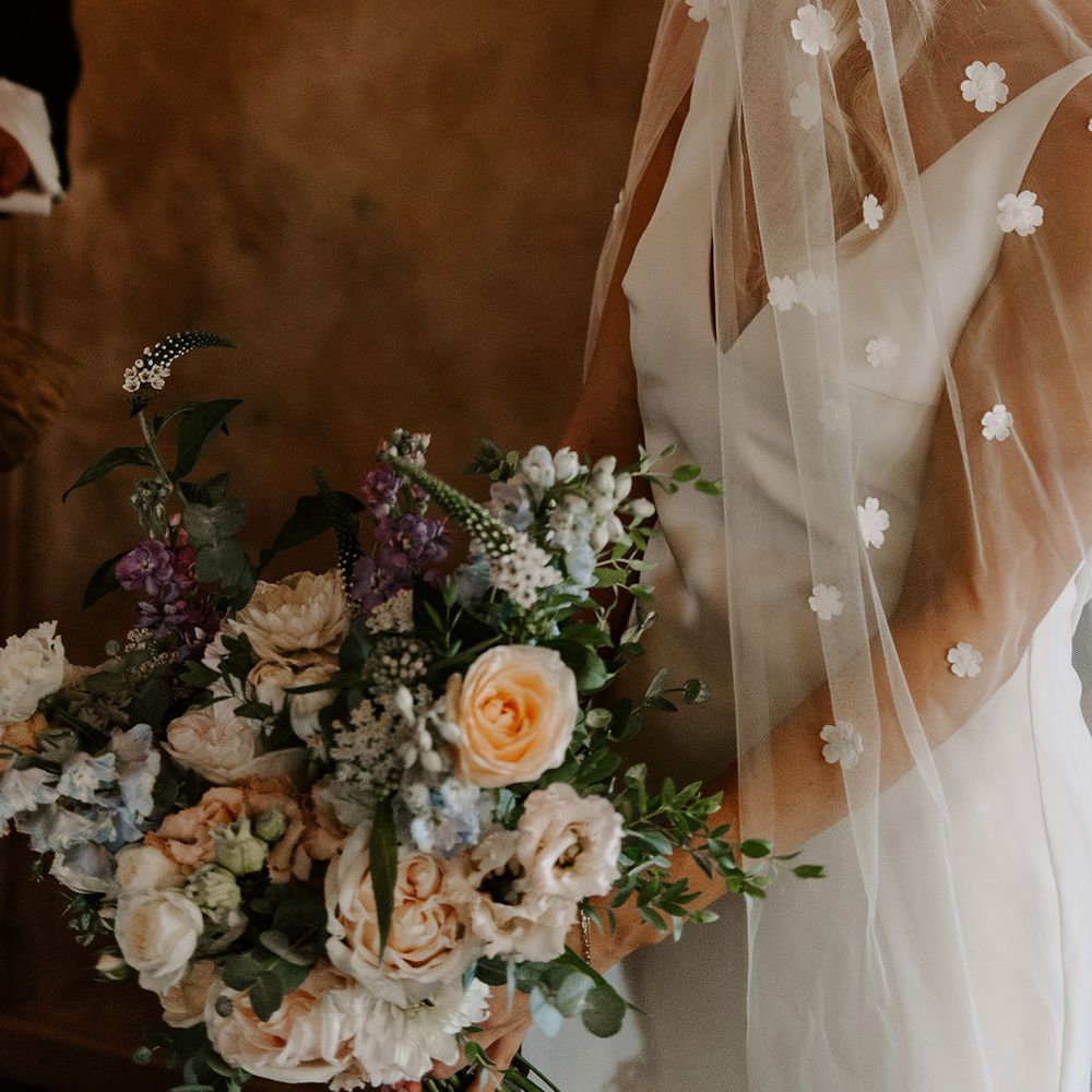 Bride holding a mixed floral bouquet with different colours in a Made With Love wedding dress and flower applique veil 
