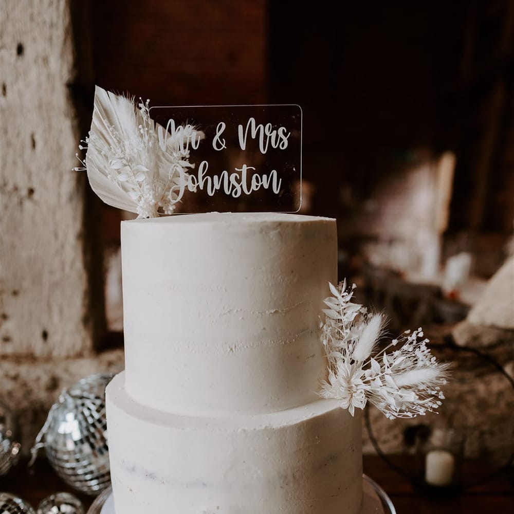 Two tier white frosted wedding cake with dried flower decor and personalised acrylic cake topper 