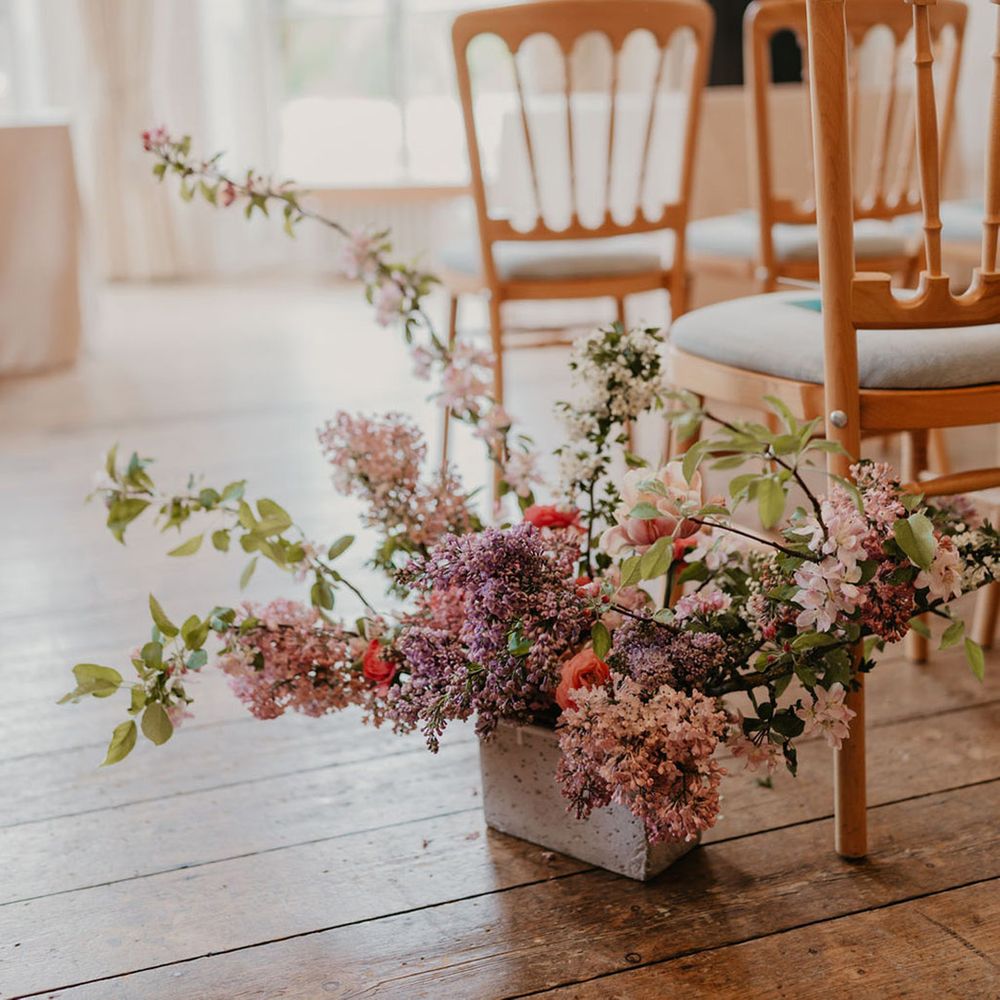 Bright floral arrangements line the aisle beside wooden chairs of Kew Gardens wedding 