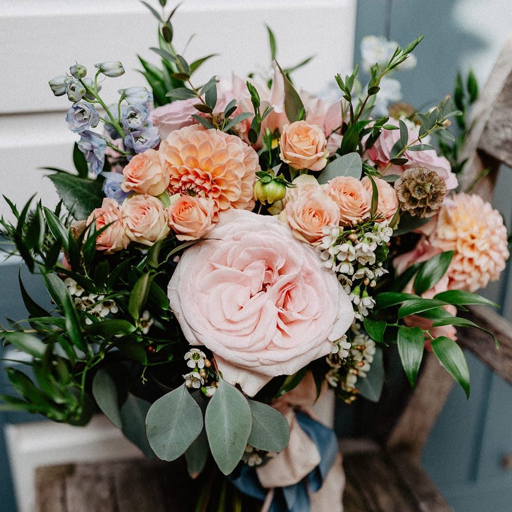 Spring wedding bouquet with blue, peach and pink wedding flowers including wax flower, roses and dahlias 