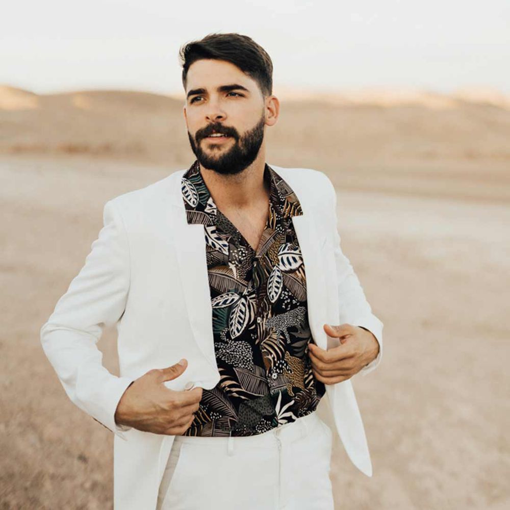 Groom in alternative groom suit; white suit and dark patterned shirt - wedding budget spreadsheet options 
