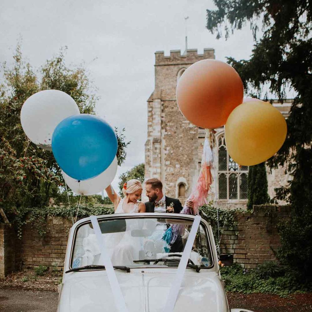 Classic convertible wedding car with white ribbon and large colourful balloons 