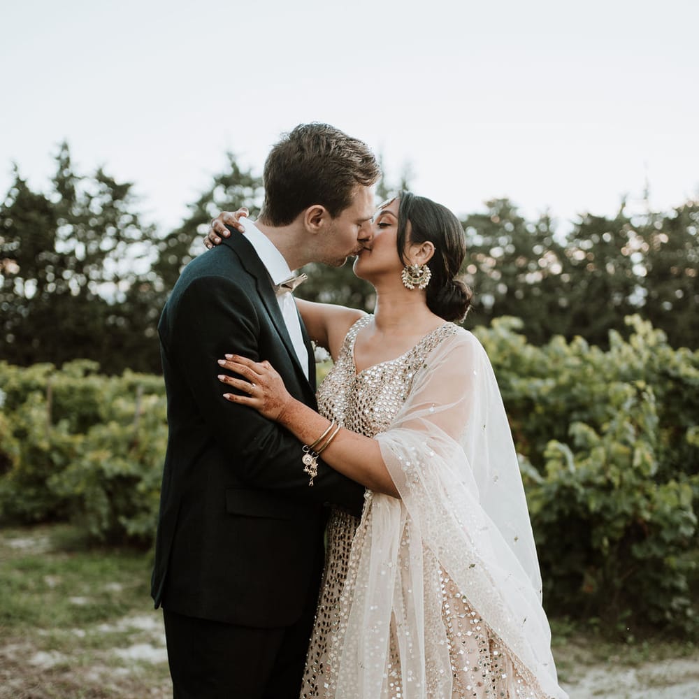 Groom in a black tuxedo kissing his bride in a sparkly wedding dress at their Domaine de Blanche Fleur destination wedding 