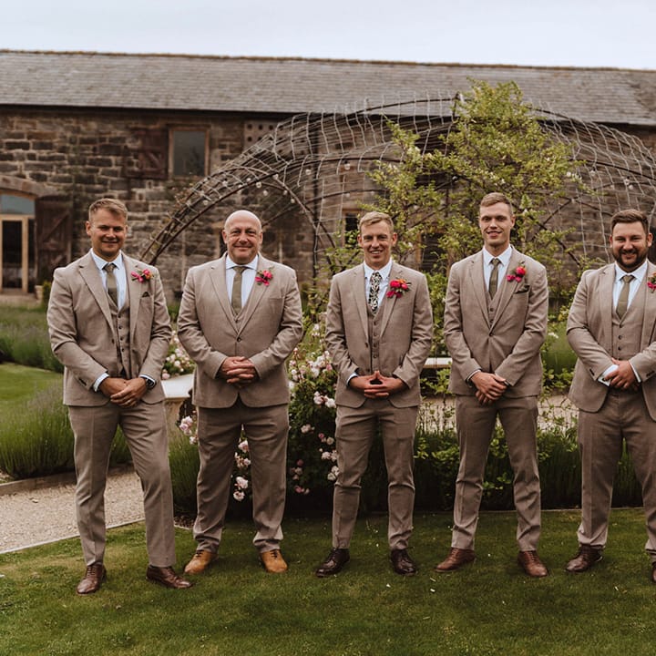 The groom and groomsmen all wear matching beige three piece suits with the groom wearing a different funky floral tie from Peggy and Finn
