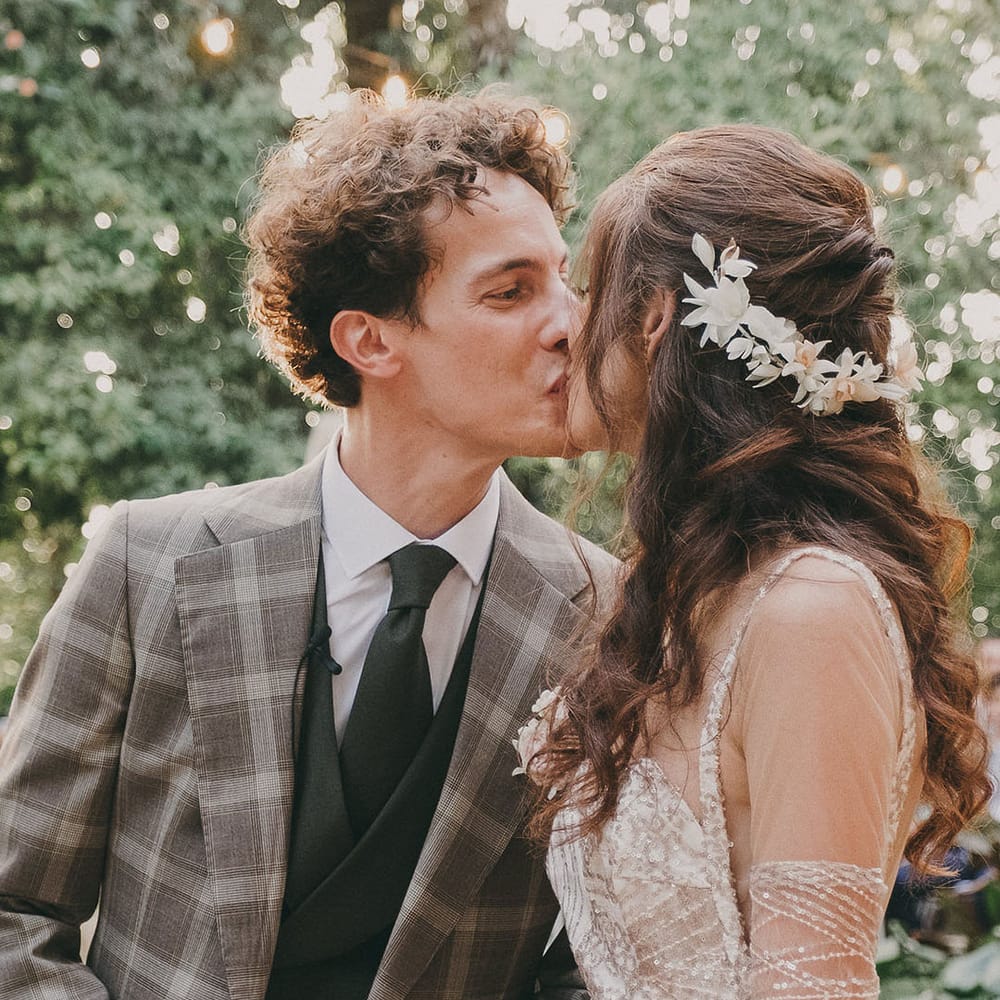 groom in a check suit kissing his bride in a gold sparkly wedding dress and dried flower hair accessory 