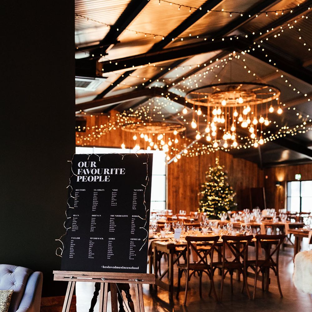 Cosy fairy lights, big festoon lights, and Christmas tree at Silchester Farm with black and white wedding table plan sign 