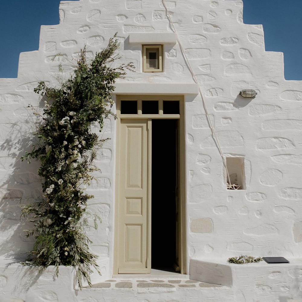 White wedding chapel in Paros, Greece at destination wedding with green and white flower arrangements