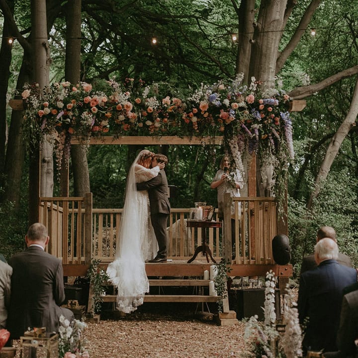 The bride and groom share their first kiss as a married couple at their outdoor humanist wedding ceremony in the woods