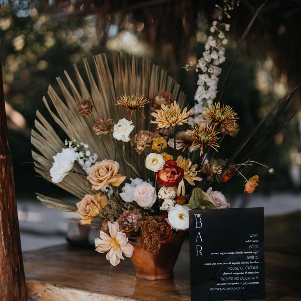 White, orange and burnt orange dried flower arrangements in ceramic vase with monochrome minimalistic bar sign 