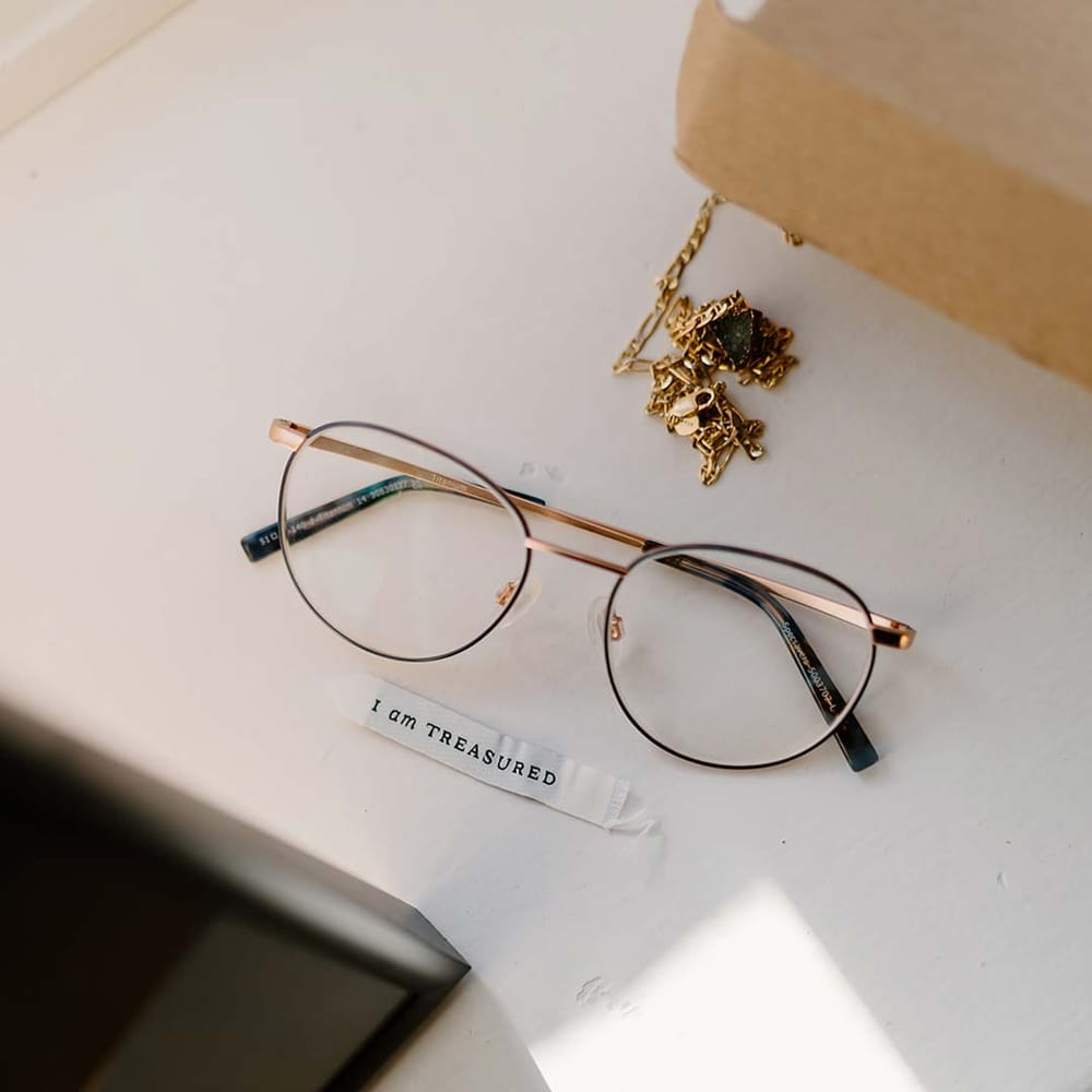 Gold rimmed grooms glasses with gold bridal jewellery and wedding affirmations printed on paper at Broadfield Court wedding venue