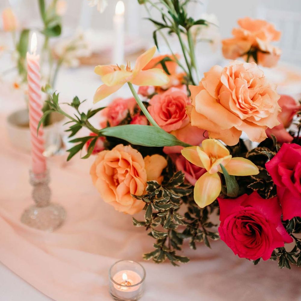 Wedding table with pastel pink twisted tapered candles, tea light candles and flower arrangement centrepiece with pink and orange garden roses, orange floribunda, yellow ranunculus flowers, foliage and Iceland poppies 