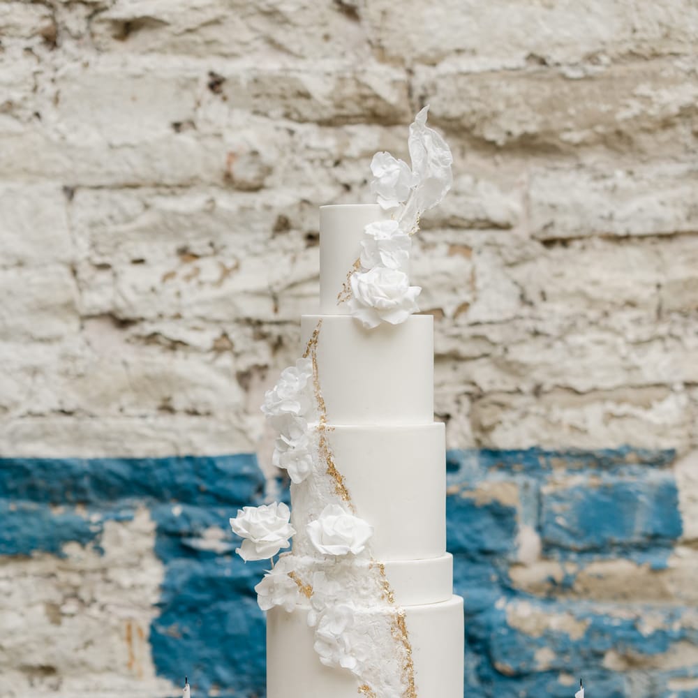Elegant five tier white wedding cake with different size layers and floral decor and gold design 