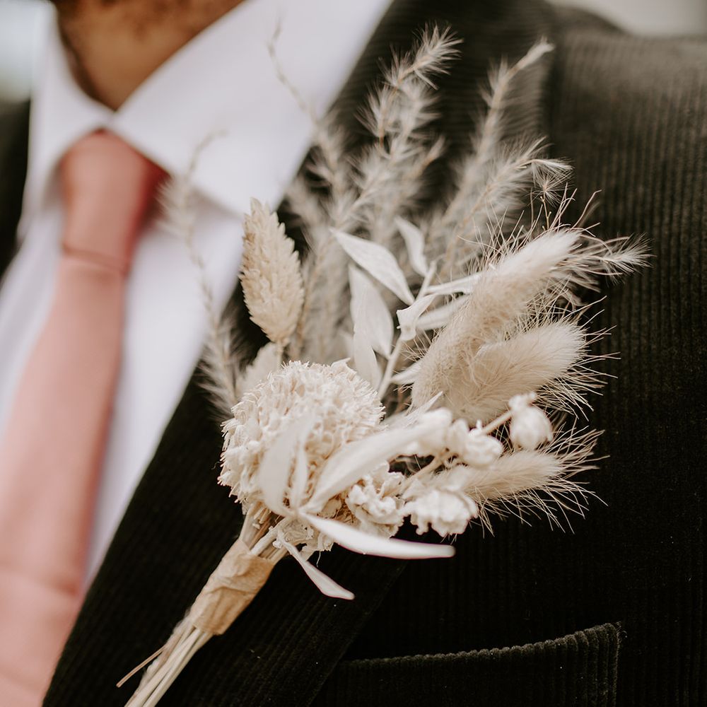 Groom in a black suit and pink tie with a neutral dried flower buttonhole 
