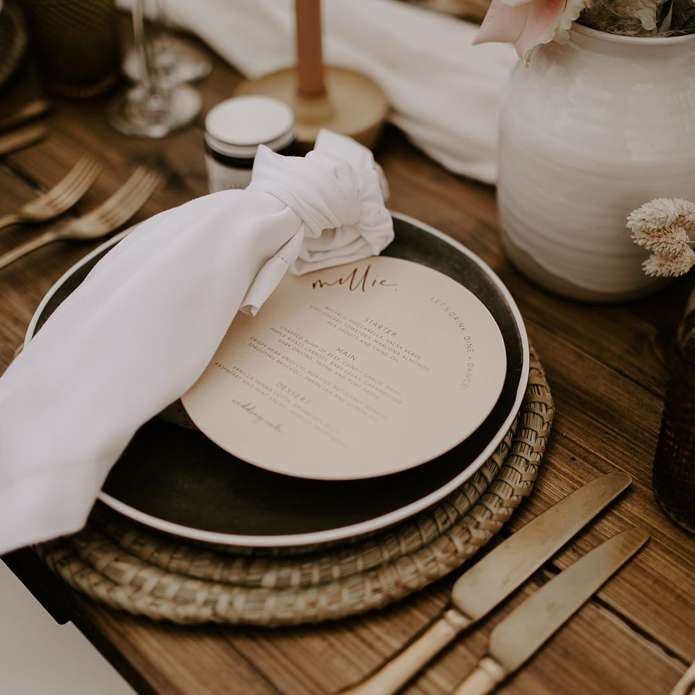 Place setting with wicker place mat, gold cutlery, napkins and circular menu card 
