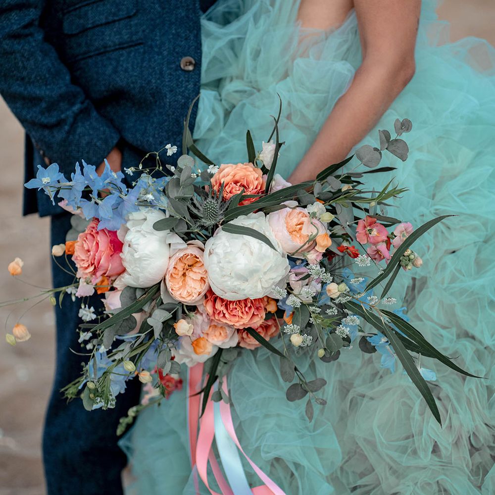 Bride in coloured tulle wedding dress holding a white, peach, pink and green wedding bouquet by her side