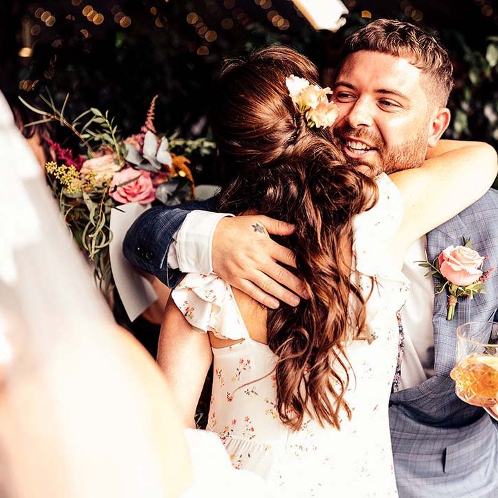 Bridesmaid hugs groom in blue check suit after the Stone Barn Cotswolds wedding ceremony 
