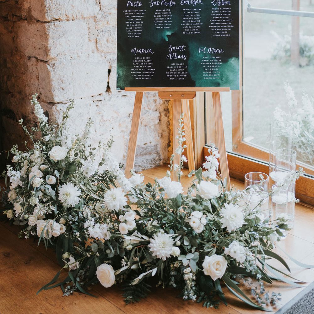 Green acrylic wedding table plan on wooden easel with white and green floral garland and candles for elegant wedding at Notley Abbey