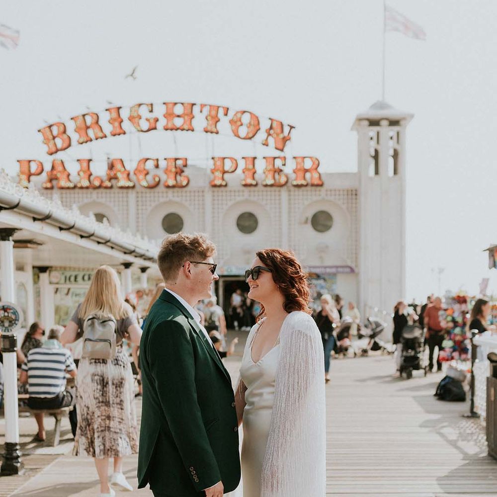 Bride & groom look lovingly at one another in front of Brighton Pier on their wedding day