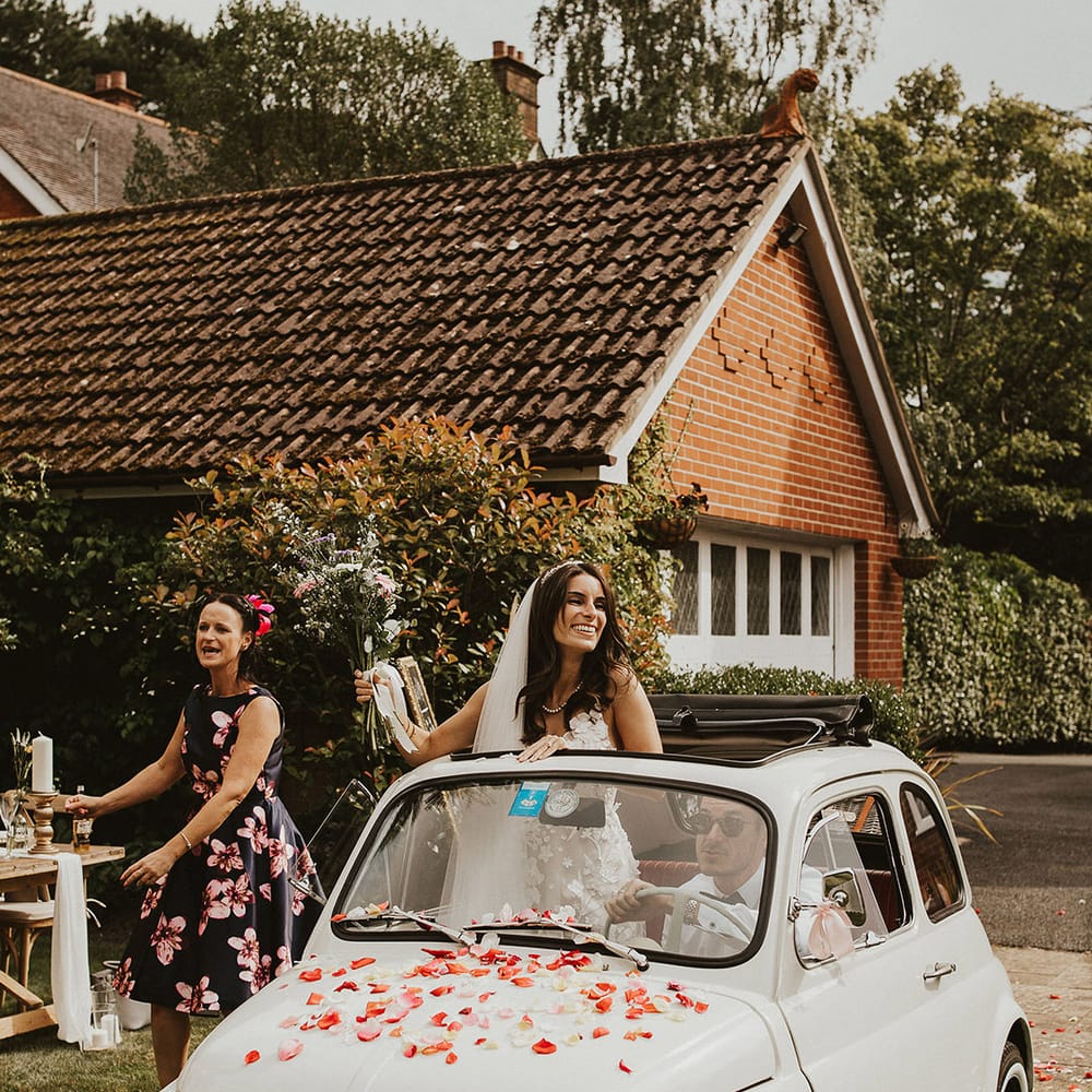 Bride sits in Fiat 500 as she dances out of sunroof on her wedding day