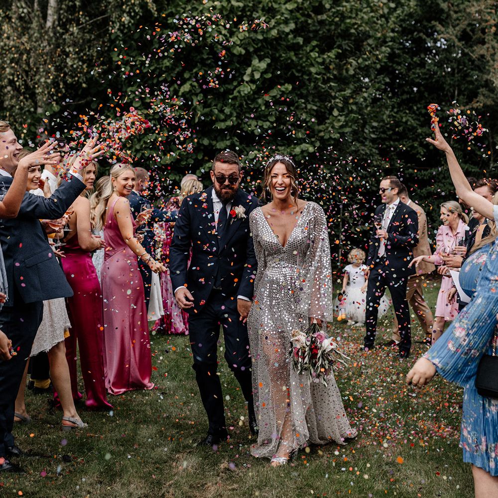 Colourful confetti moment with bride in a silver sequin wedding dress and groom in a navy suit at back garden wedding 