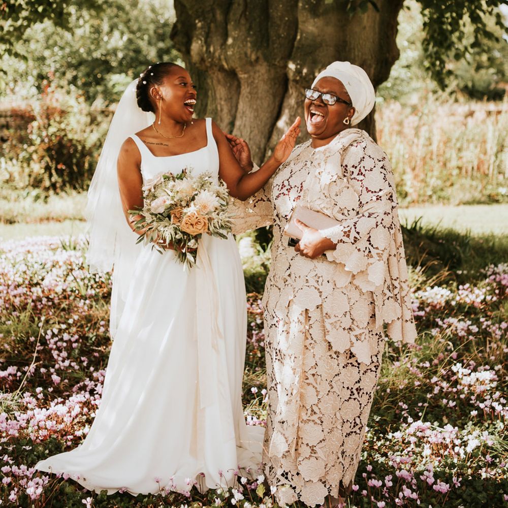 Black bride and mother of the bride laughing together under a tree at Elmore Court 