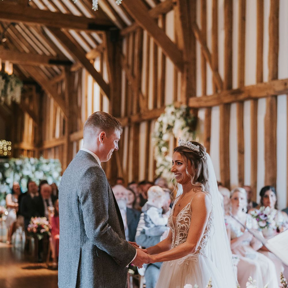 Bride in jewelled silver tiara and groom at the end of the aisle in rustic wedding venue complete with hanging wisteria 
