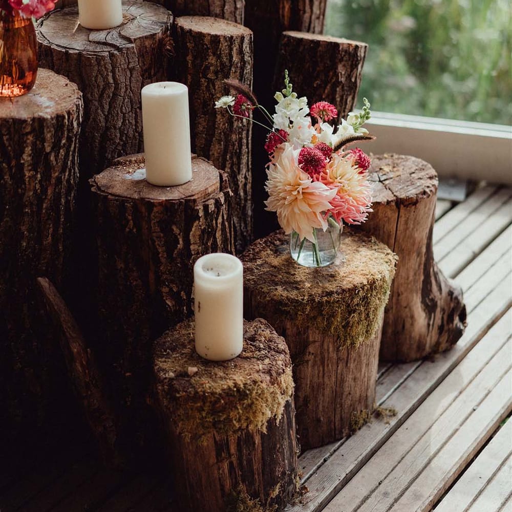 Wedding decor with tree trunks and white pillar candles with pink, red and white flowers 