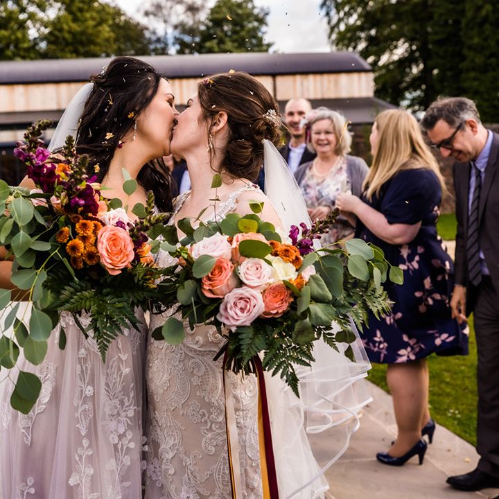 Brides share a kiss after having their confetti exit from their wedding ceremony