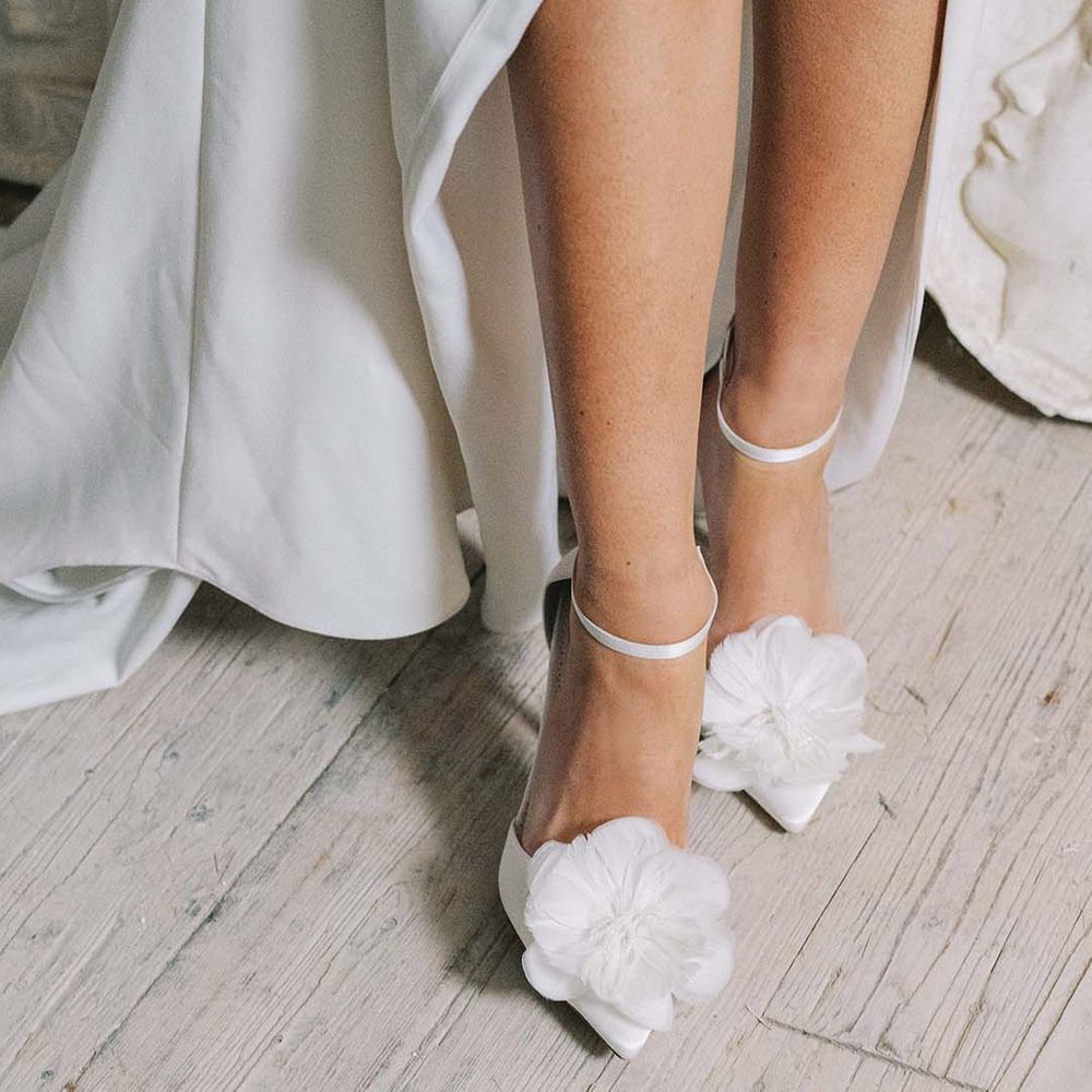 Bride wearing white stiletto wedding shoes with ankle strap and feather flower with beads from Bella Belle 