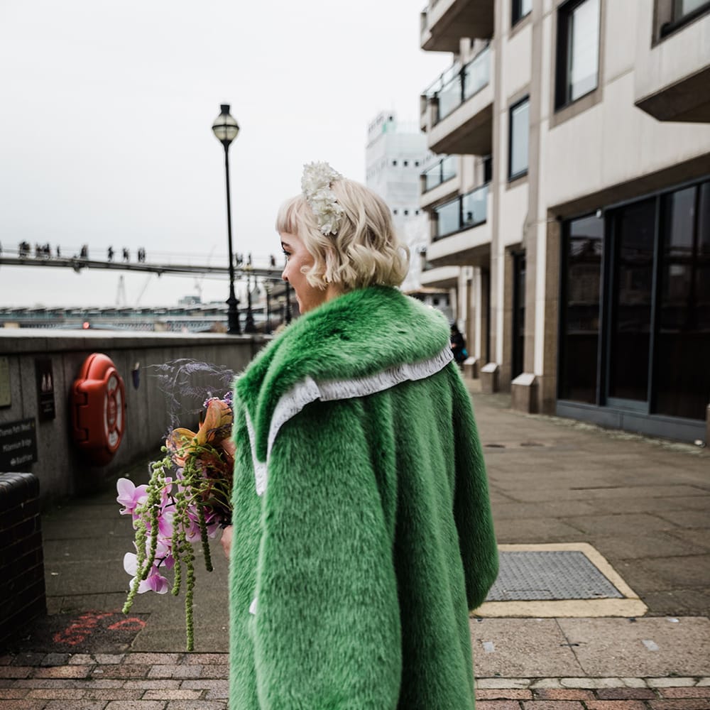 Bride with short blonde hair and white flower headband wearing green fur coat with velvet platform block heels