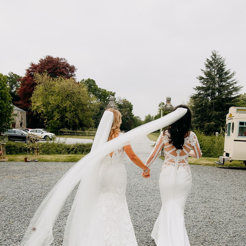 brides walk holding hands together with veils blowing in the breeze