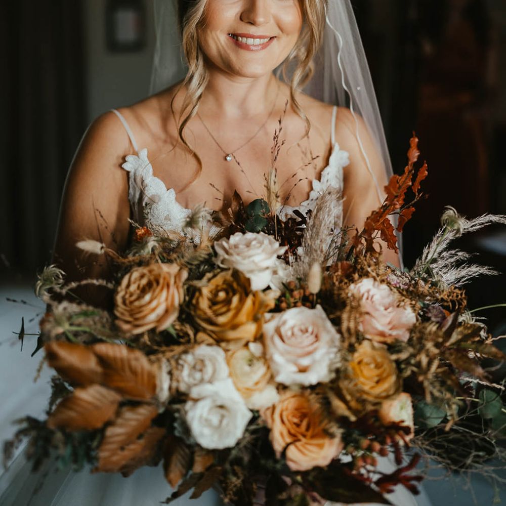 Bride with warm toned eyeshadow holding matching warm toned autumnal wedding bouquet for her autumn wedding 