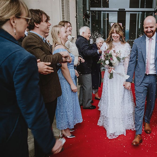 Bride & groom walk along red carpet outside St. George's Hall as confetti is thrown around them by friend and family 