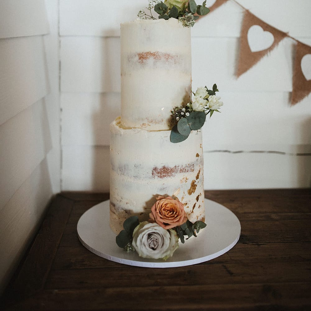 Two tier naked frosted wedding cake complete with white floral decor