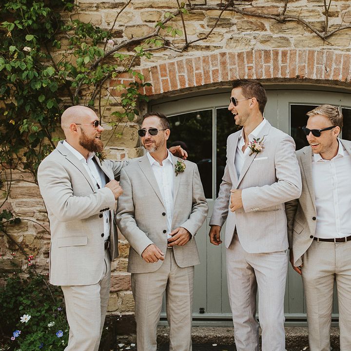 Groom smiles with the groomsmen as they all wear sunglasses and matching pale suits 