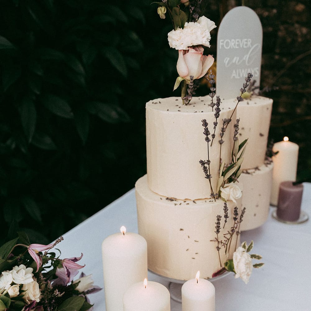 White and lavender pillar candles with three tier buttercream cake with lavender and white rose decorations
