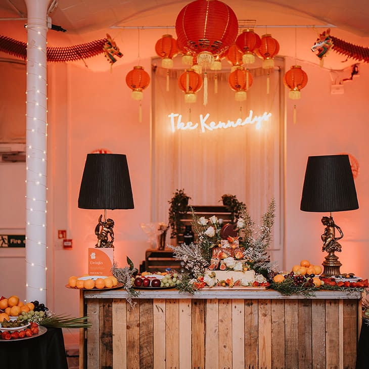 Wedding cheese tower with foliage, baby's breath and seasonal fruit decorations at London wedding with Chinese lanterns hanging above and personalised neon light