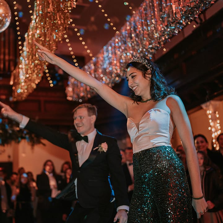 Bride in taffeta sweetheart neckline wedding top and dark green sequin disco trousers and groom in black tux having a dance at their wedding disco