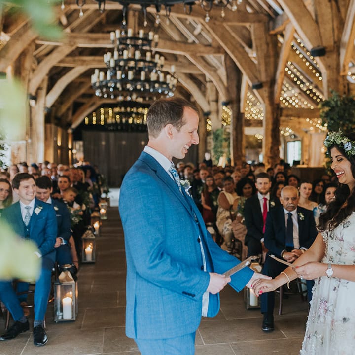 Bride in a floral wedding dress and groom in a blue suit exchanging personalised wedding vows 