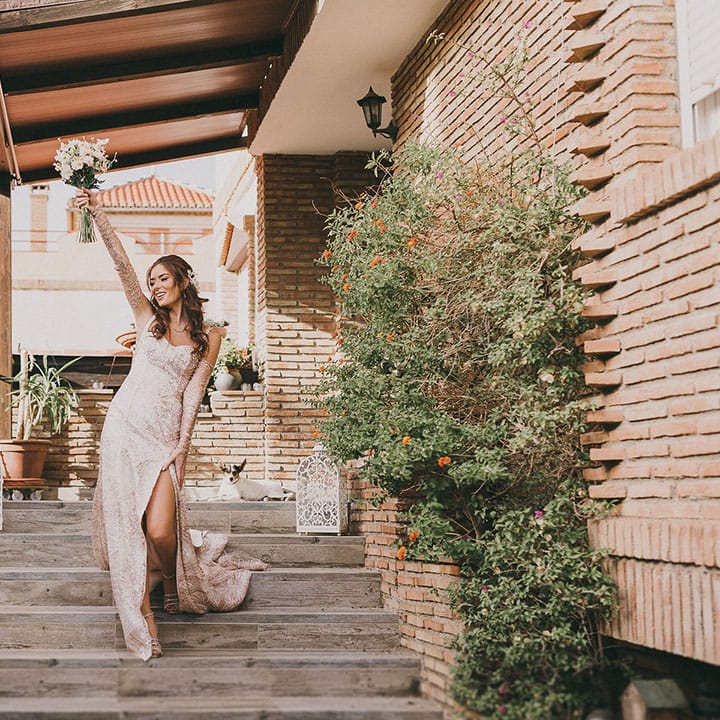 bride in a bespoke gold wedding dress with front slit holding her bouquet in the air 