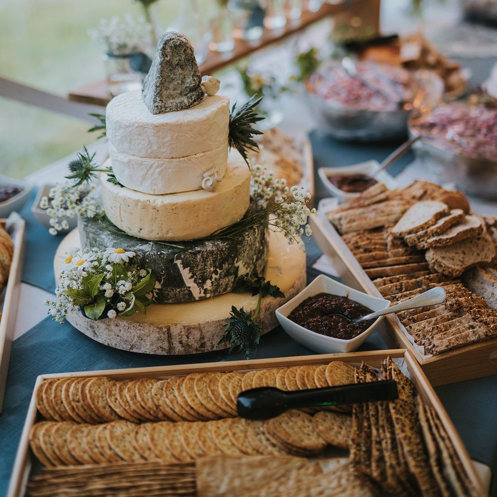 Trays of crackers and bread with bowls of chutney surround the epic cheese tower decorated with flowers for rustic marquee wedding at Badgers Holt
