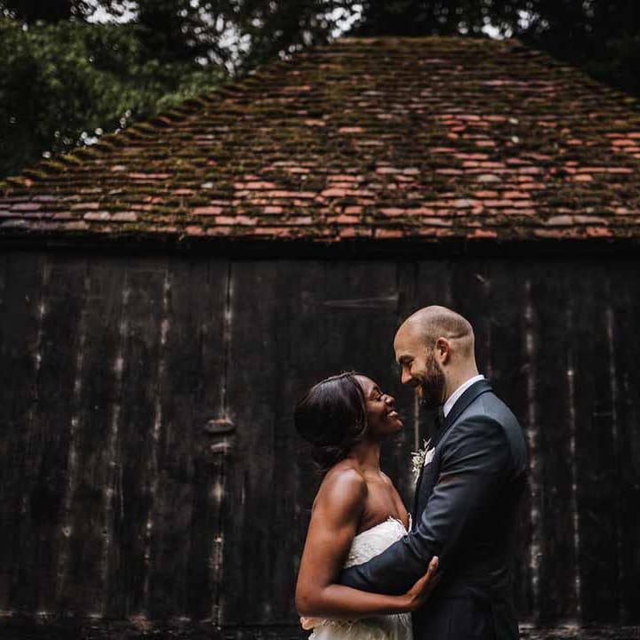 Bride in sweetheart neckline lace wedding dress and groom in classic black three piece grooms suit with bow tie and white rose and foliage boutonniere in church embracing
